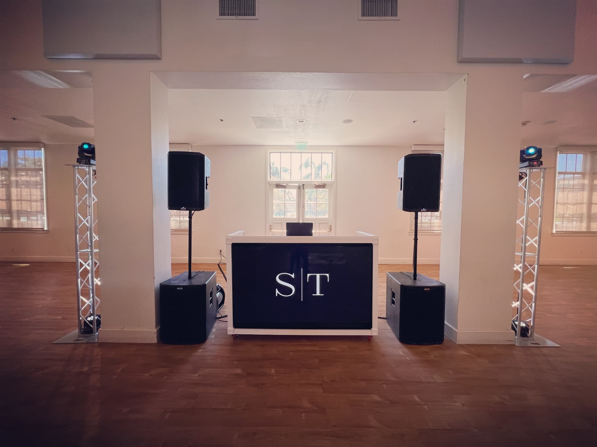 White DJ booth with subwoofers and truss lighting in a bright ballroom